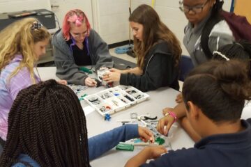 Supporting career readiness through Robotics challenges. Group of students building a robotic with various parts.